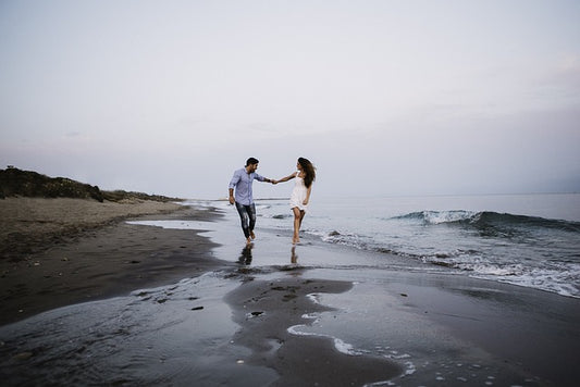 Happy couple holding hands and running along a beach, with waves gently crashing in the background at twilight