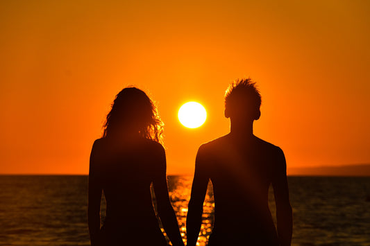 Silhouette of a couple holding hands against a vibrant sunset over the ocean